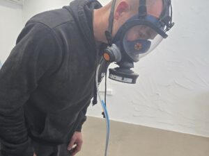 Worker leaning forward during a quantitative mask fit test while wearing a Sundström SR 200 full face respirator connected to sampling tubing.